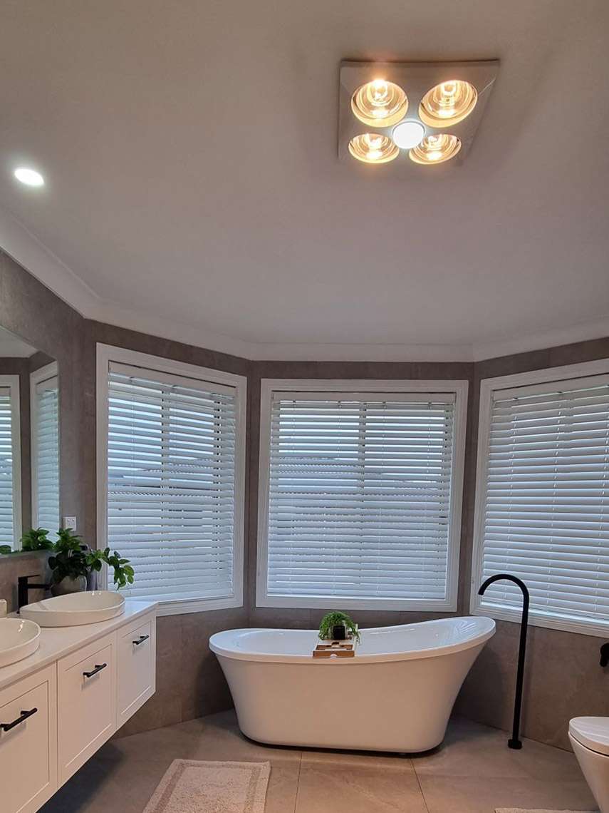 Bathroom with a freestanding bath under bay windows, a heat lamp light and white vanity