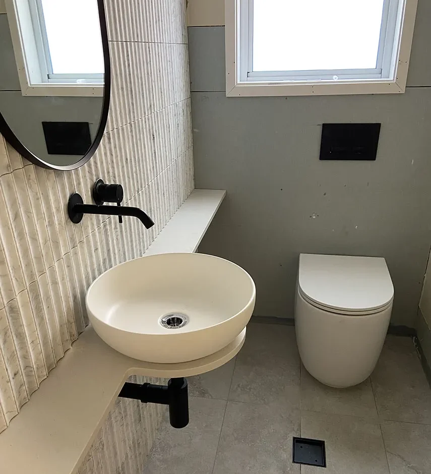 bathroom-renovations-services-western-sydney Round basin on a floating shelf against fluted wall tiles, with a mirror and toilet behind