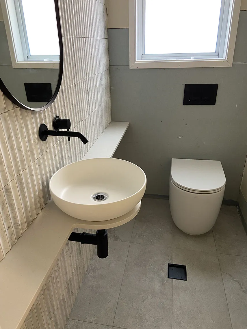 bathroom renovations services western sydney Bathroom with a round basin on a floating stone shelf, black tapware and a white toilet