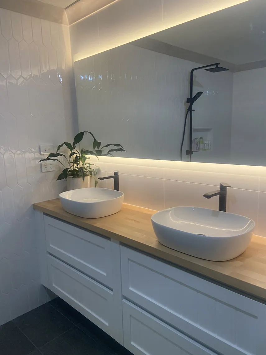 White shaker-style vanity with a timber top, two vessel basins and an LED-lit mirror