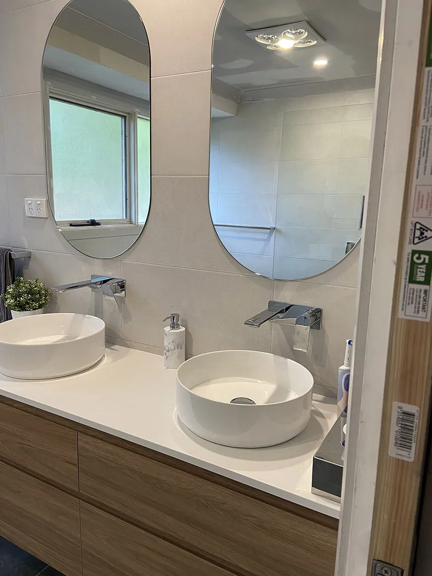 Two vessel basins on a timber-look vanity below two oval mirrors