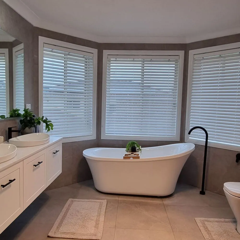residential bathroom renovation service Freestanding bath in a bay window with white blinds, a black floor-mounted tap and white vanity