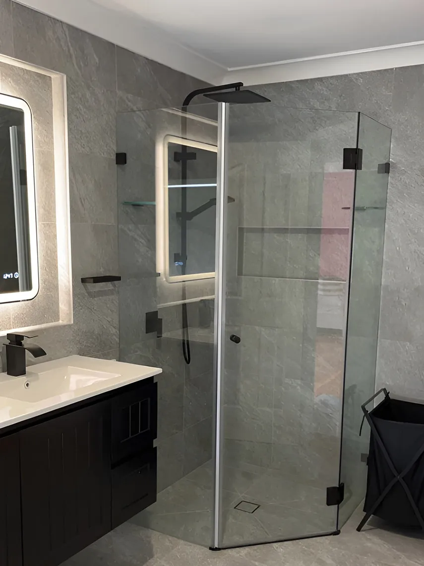 Angled frameless shower screen with black hinges in a grey-tiled bathroom