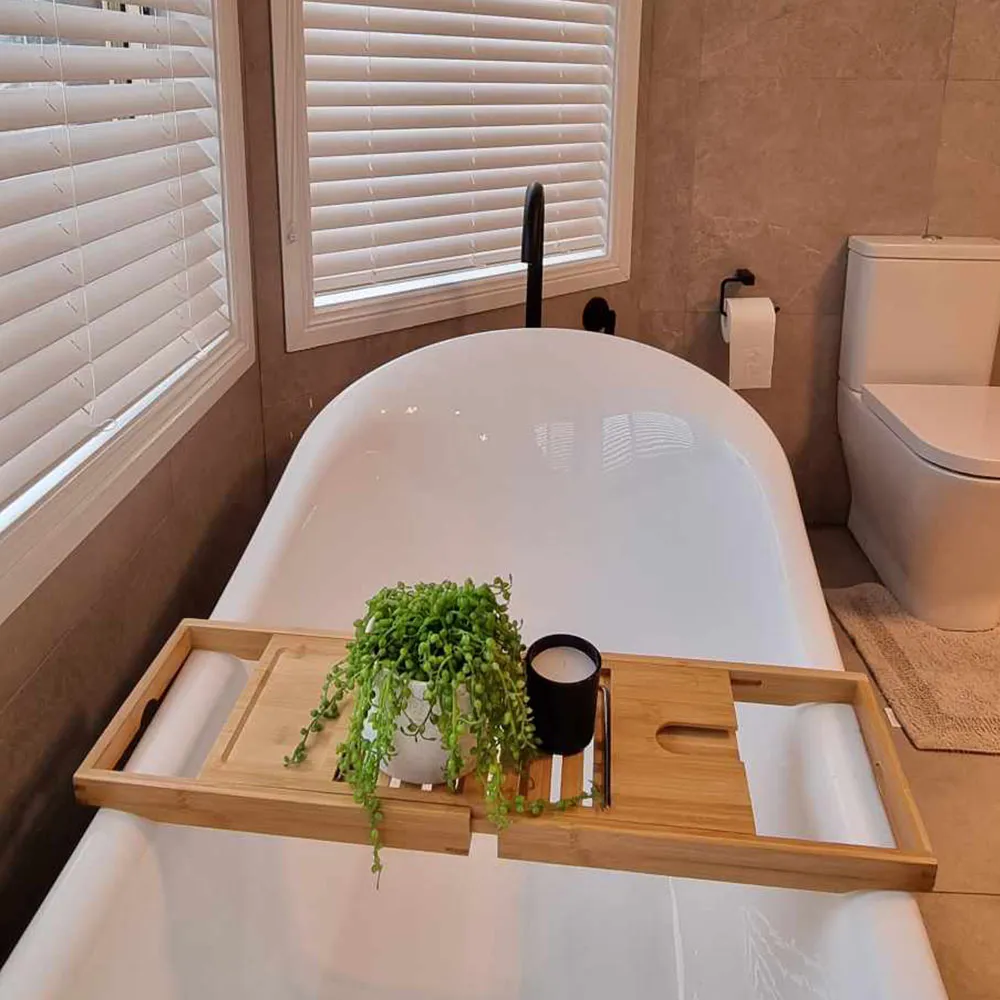 western sydney bathroom renovators Freestanding bath with a bamboo bath caddy holding a plant, beside windows with white blinds